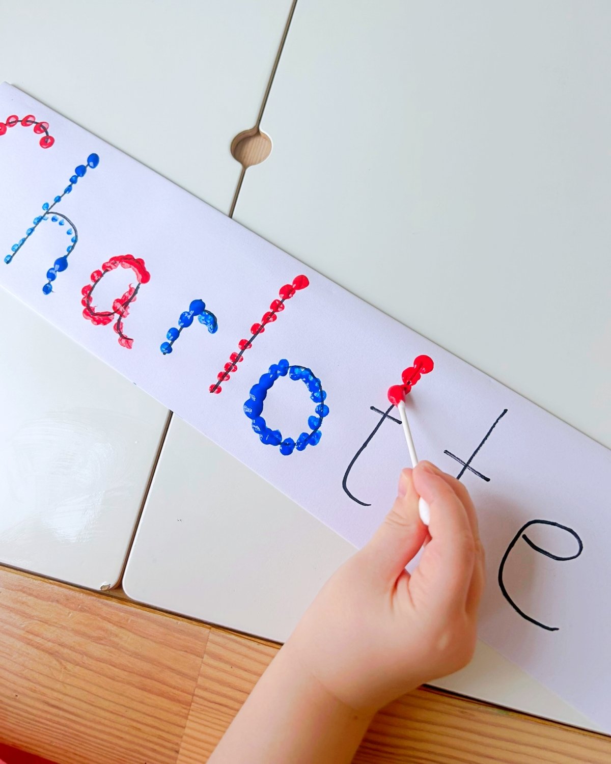child uses a cotton bud to paint and follow the lines of letters in her name